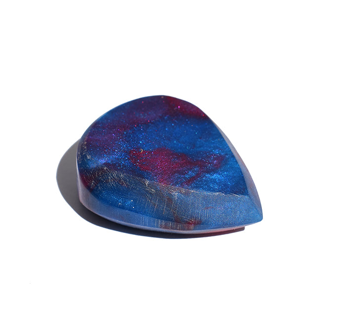 Left side angle of blue and red swirl resin guitar pick showing bevel profile