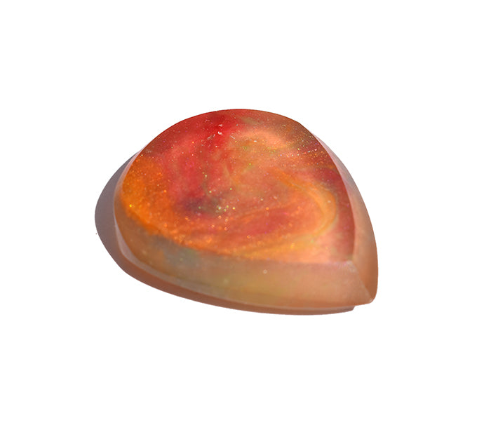 Left side angle of a polished thick resin guitar pick featuring a marbled pattern of vibrant red, orange, and soft peach tones 
